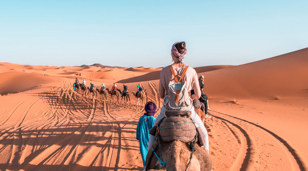 Girl riding a camel in Morocco with blue sky and sand dunes.